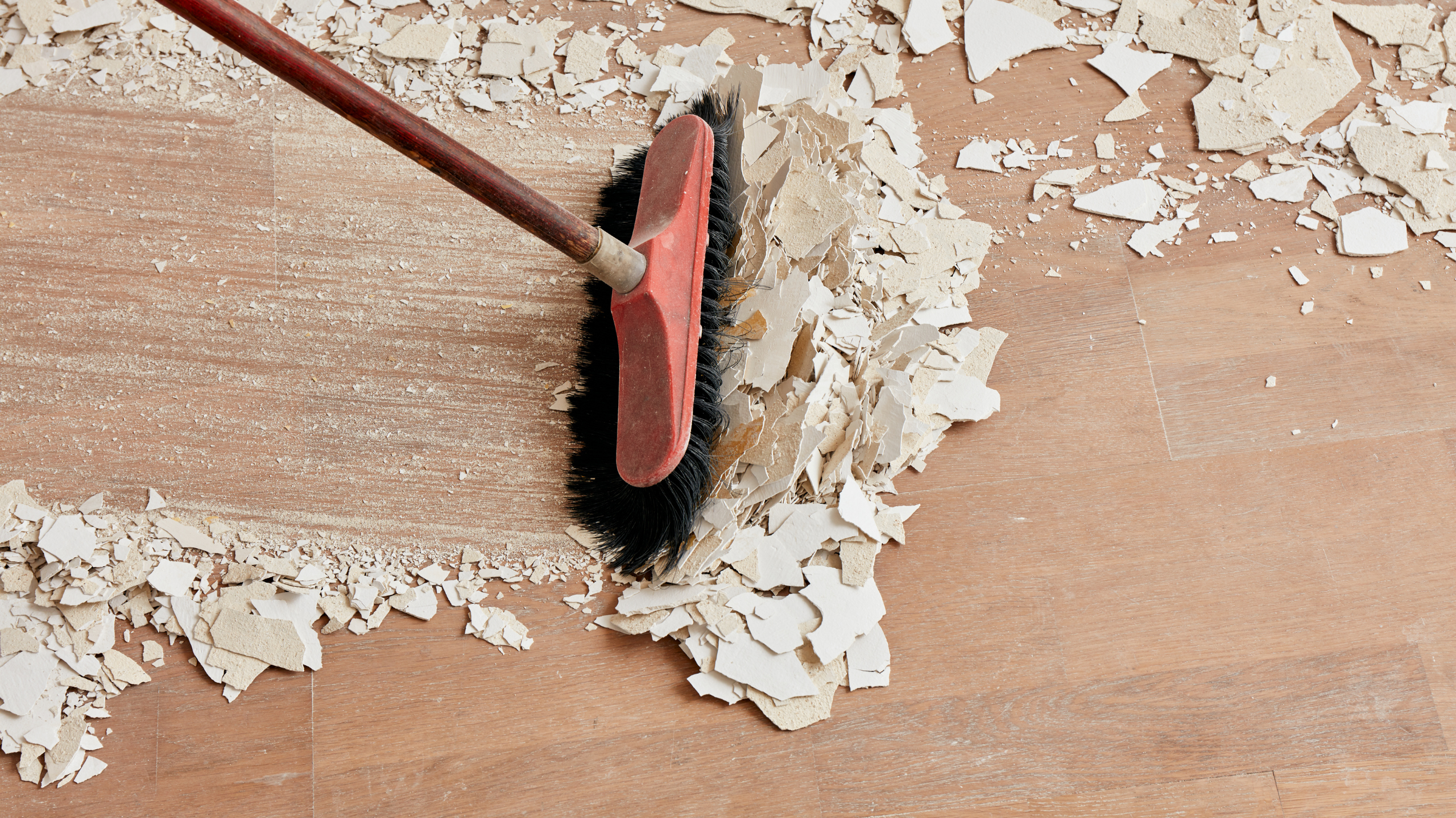A broom sweeping debris on a wooden floor, visually representing the detailed work involved in after builders cleaning